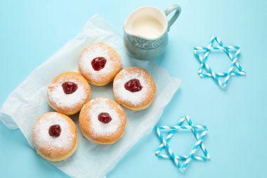 Hanuka tatlı donutları sufganiyot (geleneksel çörekler), meyveli reçel ve mavi kağıtta beyaz mumlar. Yahudi bayramı Hanuka konsepti.