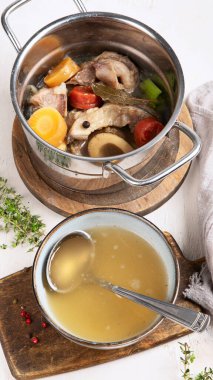 Etli et çorbası yavaş yavaş sebzelerle pişiriliyor: havuç, soğan, sarımsak ve baharatlar beyaz bir arka planda, malzemelerle servis ediliyor..