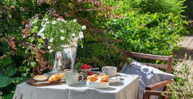 Bahçe masasında Avrupalı kahvaltısı. Taşra yaşam tarzı ya da hafta sonu sabah konsepti. Huzurlu kırsal manzara. Panorama