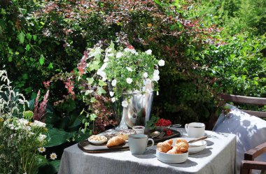 Bahçe masasında Avrupalı kahvaltısı. Taşra yaşam tarzı ya da hafta sonu sabah konsepti. Huzurlu kırsal manzara.