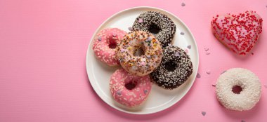 Çikolatalı donut, marşmelov ve pembe arka planda şeker serpiştirme, üst manzara. Renkli karnaval ya da doğum günü partisi kartı. Ulusal Çörek Günü 'nüz kutlu olsun. Kopyalama alanı olan Panorama.