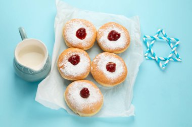 Hanuka tatlı donutları sufganiyot (geleneksel çörekler), meyveli reçel ve mavi kağıtta beyaz mumlar. Yahudi bayramı Hanuka konsepti.