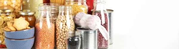 Food supplies crisis food stock. Different glass jars with grains, pasta, cans of canned food on  white background. Panorama, banner, copy spac