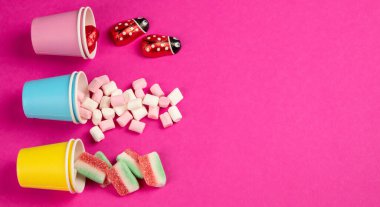 Değişik renkte tatlı jöle şekerler ve pembe arka planda eko bardaklarda şekerleme. Üst Manzara. Kopyalama alanı olan Panorama.