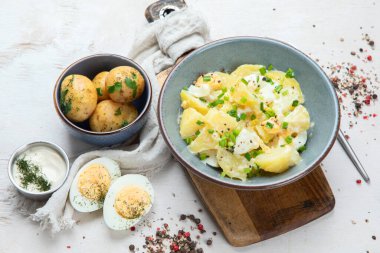 Beyaz arka planda bir tabakta patates, yumurta, yeşil soğan ve mayonez salatası.