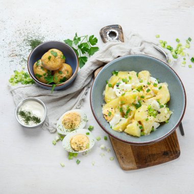 Beyaz arka planda bir tabakta patates, yumurta, yeşil soğan ve mayonez salatası.