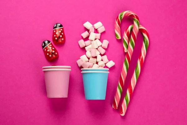 Assorted multicolored sweet jelly candies and marshmallows in eco cups on pink background. Top view.