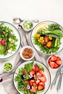 Beyaz arka planda yenilebilir çiçekler, sebzeler, meyveler, mikroyeşiller ve peynirli lezzetli bahar salataları. Temiz ve sağlıklı yeme konsepti. Üst görünüm.