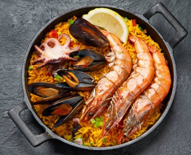 İspanya 'nın klasik yemeği, geleneksel tavada deniz ürünleri paella' sı koyu arka planda, üst manzara. İspanyol paellası, karides, kıskaç, midye, yeşil bezelye ve taze limon dilimleri. Boşluğu kopyala.