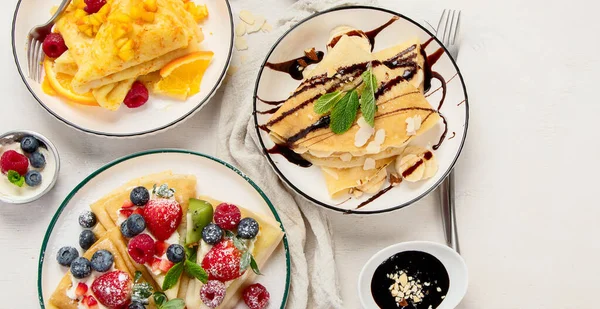 stock image Variety of fresh crepes with chocolate, jam, fruits and berries on white background. Homemade delicious crepes. Top view.