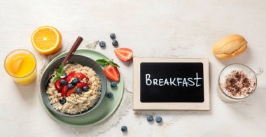 Çilekli yulaf lapası, badem ve muzlu kase. Beyaz arka planda kapuçino ve portakal suyu ile sağlıklı bir kahvaltı. Üst Manzara. Kopyalama alanı olan Panorama.