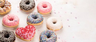 Donut deseni. Çeşit çeşit jöleli donutların üst görüntüsü. Kremalı renkli çörekler. Açık arkaplan üzerine serpiştirilmiş çeşitli renkli donutlar. Kopyalama alanı olan Panorama.