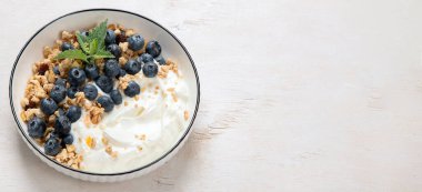 Sağlıklı kahvaltı için yoğurt ve böğürtlenli granola. Beyaz arka planda bir kase yaban mersini ve ahududu içeren Yunan yoğurdu. Kopyalama alanı olan Panorama.