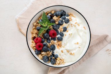 Sağlıklı kahvaltı için yoğurt ve böğürtlenli granola. Beyaz arka planda, yaban mersini ve ahududu aromalı bir kase Yunan yoğurdu..