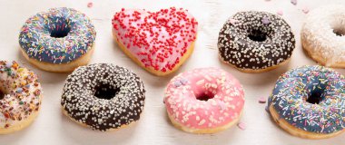 Donut deseni. Çeşit çeşit jöleli donutların üst görüntüsü. Kremalı renkli çörekler. Açık arkaplan üzerine serpiştirilmiş çeşitli renkli donutlar. Panorama.