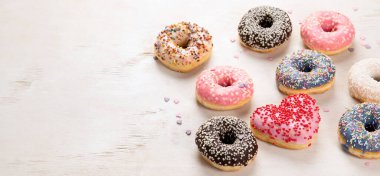 Donut deseni. Çeşit çeşit jöleli donutların üst görüntüsü. Kremalı renkli çörekler. Açık arkaplan üzerine serpiştirilmiş çeşitli renkli donutlar. Kopyalama alanı olan Panorama.