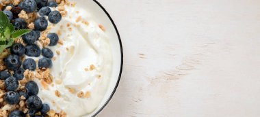 Sağlıklı kahvaltı için yoğurt ve böğürtlenli granola. Beyaz arka planda bir kase yaban mersini ve ahududu içeren Yunan yoğurdu. Kopyalama alanı olan Panorama.