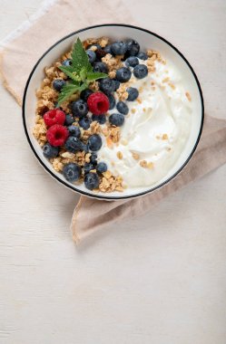 Sağlıklı kahvaltı için yoğurt ve böğürtlenli granola. Beyaz arka planda bir kase yaban mersini ve ahududu içeren Yunan yoğurdu. Boşluğu kopyala.