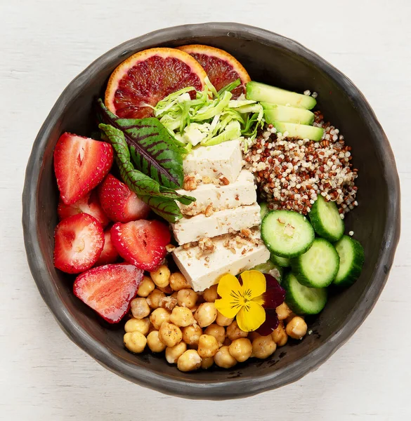 Sağlıklı vejetaryen yemek kasesi. Avokado, kinoa, salatalık, kırmızı portakal, nohut, peynir, salata ve beyaz arka planda çilek. Üst görünüm.