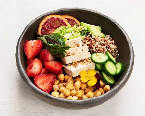 Sağlıklı vejetaryen yemek kasesi. Avokado, kinoa, salatalık, kırmızı portakal, nohut, peynir, salata ve beyaz arka planda çilek. Üst görünüm.