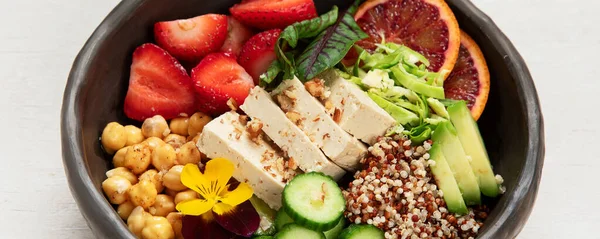 Sağlıklı vejetaryen yemek kasesi. Avokado, kinoa, salatalık, kırmızı portakal, nohut, peynir, salata ve beyaz arka planda çilek. Üst görünüm.