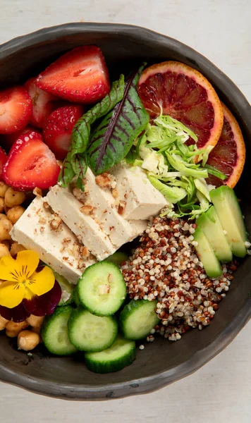 Sağlıklı vejetaryen yemek kasesi. Avokado, kinoa, salatalık, kırmızı portakal, nohut, peynir, salata ve beyaz arka planda çilek. Üst görünüm.