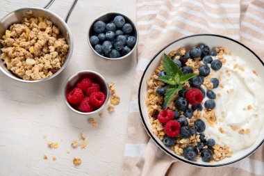 Sağlıklı kahvaltı için yoğurt ve böğürtlenli granola. Beyaz arka planda, yaban mersini ve ahududu aromalı bir kase Yunan yoğurdu..