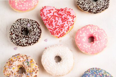 Donut deseni. Çeşit çeşit jöleli donutların üst görüntüsü. Kremalı renkli çörekler. Açık arkaplana serpiştirilmiş çeşitli renkli donutlar..