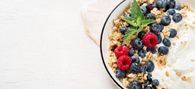 Sağlıklı kahvaltı için yoğurt ve böğürtlenli granola. Beyaz arka planda bir kase yaban mersini ve ahududu içeren Yunan yoğurdu. Kopyalama alanı olan Panorama.
