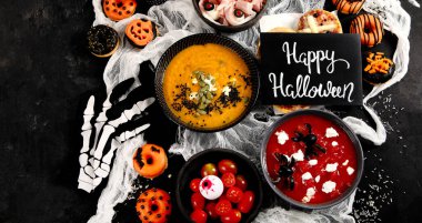 Cadılar Bayramı için eğlenceli bir parti masası. Pizza, balkabağı çorbası, şeker, göz küresi spagettisi, siyah arka planda aperatifler ve çörekler. Üst görünüm.