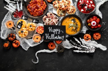 Cadılar Bayramı için eğlenceli bir parti masası. Pizza, balkabağı çorbası, şeker, göz küresi spagettisi, siyah arka planda aperatifler ve çörekler. Üst görünüm.