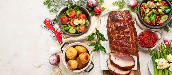 Concept of Christmas or New Year dinner with roasted meat and various vegetables dishes on a white background. Top view. Panorama with copy space.