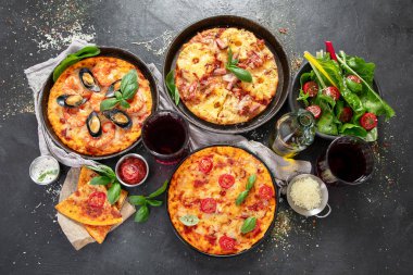 Pizza partisi yemeği. Üzerinde çeşitli İtalyan pizzası, salata ve kırmızı şarap bulunan bir masa.. 