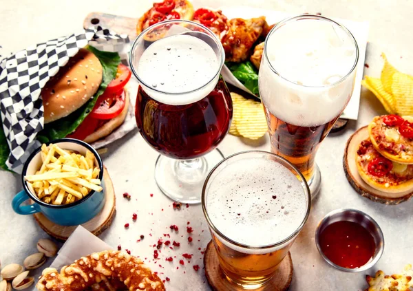 Fast food dish. Juicy burger, chicken wings, snacks, sauces and glasses of cold beer on light background. Top view.