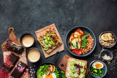 Avokado tostlu lezzetli yemekler, sebzeler, koyu arkaplanda yumurtalar. Helthy kahvaltı konsepti. Üst görünüm, alanı kopyala.