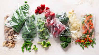 Beyaz arka planda plastik poşetlerde farklı donmuş sebzeler. Üst görünüm.