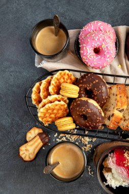 Lezzetli kurabiyeli beyaz kahve, çörek, kek, şeker, waffle. Karanlık arka planda şekerli sıcak içecek. Üst görünüm, alanı kopyala.