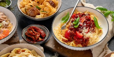 Makarna. İtalyan makarna yemekleri. Siyah arka planda spagetti bolonez, makarna, tortellini, ravioli ve diğerleri de var. Üst görünüm.