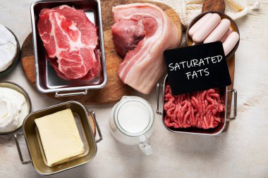 Masalarda doymuş yağlar. Çiğ et, sosis, peynir, tereyağı. Kötü yemek konsepti. Üst görünüm