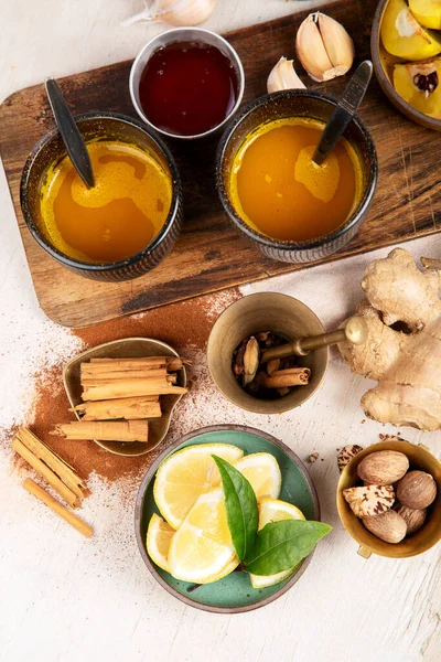 Cups of healthy turmeric spice tea with ingredients: lemon, ginger, cinnamon sticks and honey on a white background, top view. Immune boosting remedy.