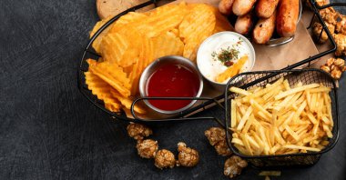 Sepetlediğim sağlıksız yiyecekler. TV uzaktan kumandası ve atıştırmalıklar - cips, patlamış mısır, kurabiye, peynir, sos, patates kızartması, pizza. Üst görünüm, alanı kopyala