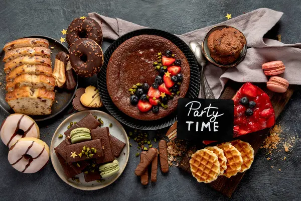 Tasty cake, cookies, waffles, macaroons, muffin. Delicious desserts on dark background. Food concept. Top view