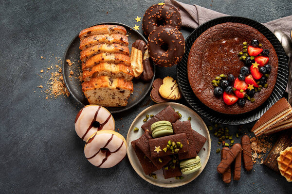 Tasty cake, cookies, waffles, macaroons, muffin. Delicious desserts on dark background. Food concept. Top view, copy space.