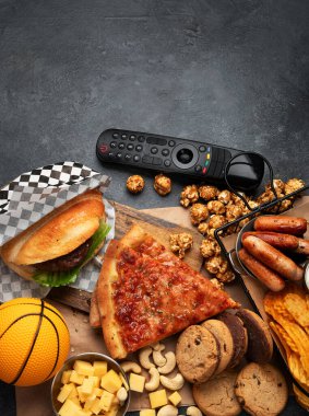 Sepetlediğim sağlıksız yiyecekler. TV uzaktan kumandası ve atıştırmalıklar - cips, patlamış mısır, kurabiye, peynir, sos, patates kızartması, pizza. Üst görünüm, alanı kopyala.