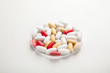 Petri kabında beyaza izole edilmiş çeşitli renkli haplar. Sağlık hizmetleri desteği. Eczane laboratuarı ve ilaç araştırma konsepti.