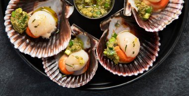 Koyu arkaplanda, siyah taş bir tabakta, soslu ve baharatlı deniz kabuklarıyla pişirilmiş deniz tarakları. Deniz ürünleri. Üst görünüm.