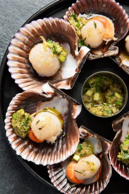 Koyu arkaplanda, siyah taş bir tabakta, soslu ve baharatlı deniz kabuklarıyla pişirilmiş deniz tarakları. Deniz ürünleri. Üst görünüm.