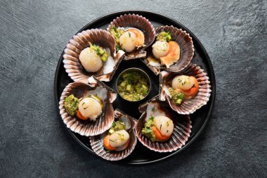 Koyu arkaplanda, siyah taş bir tabakta, soslu ve baharatlı deniz kabuklarıyla pişirilmiş deniz tarakları. Deniz ürünleri. Üst görünüm.