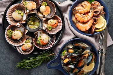 Koyu arkaplanda, siyah taş bir tabakta, soslu ve baharatlı deniz kabuklarıyla pişirilmiş deniz tarakları. Deniz ürünleri. Üst görünüm.