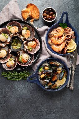 Koyu arkaplanda, siyah taş bir tabakta, soslu ve baharatlı deniz kabuklarıyla pişirilmiş deniz tarakları. Deniz ürünleri. Üst Manzara. Boşluğu kopyala.